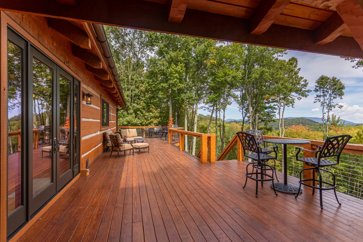 A spacious wooden deck outfitted with comfortable seating and a small metal bar table, overlooking sweeping views of the surrounding landscape. The setting suggests moments of relaxation, sunset watching, and stargazing—activities that can be enjoyed throughout the seasons.