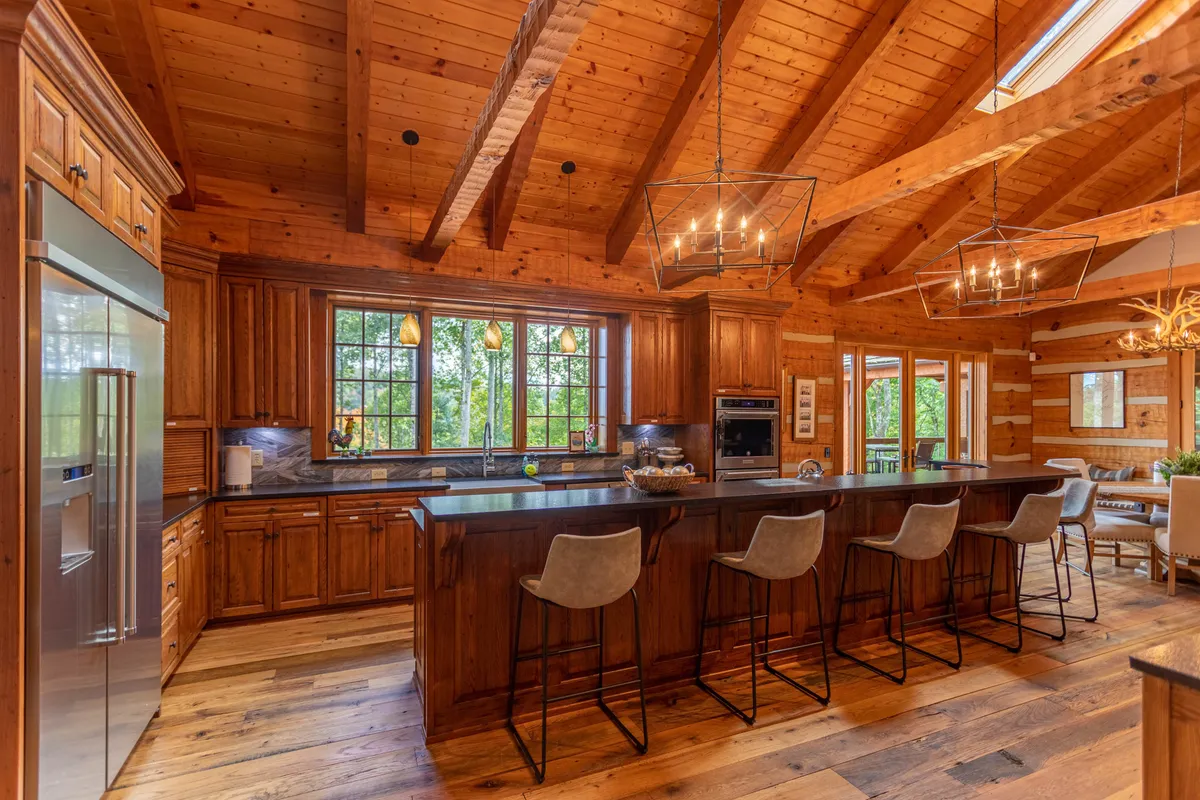A welcoming interior kitchen scene featuring a large kitchen island, warm wooden cabinetry, expansive panoramic windows that flood the space with natural light, and hanging light fixtures. The open layout invites gatherings and casual conversations.