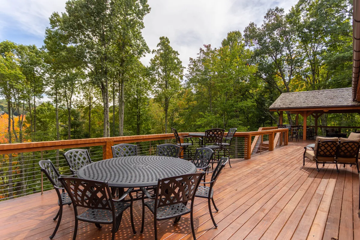 A spacious outdoor deck area set within a grove of trees, featuring a large dining table and a comfortable seating arrangement under a gazebo. The space is designed for sunset views and festive gatherings, offering a seamless blend between nature and social life.