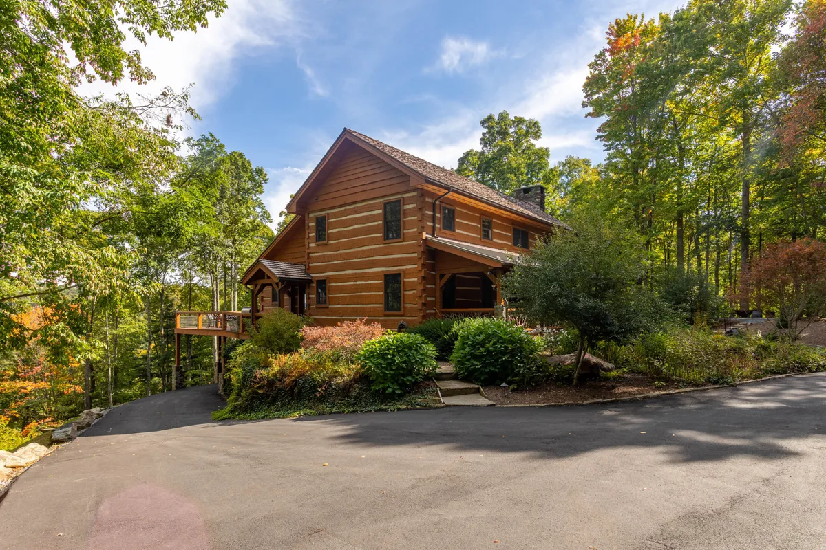 This image highlights a charming log cabin structure nestled among trees and landscaped gardens. The setting is serene and inviting, suggesting both heritage charm and a connection to nature, ideal for guests of all ages to explore and enjoy.