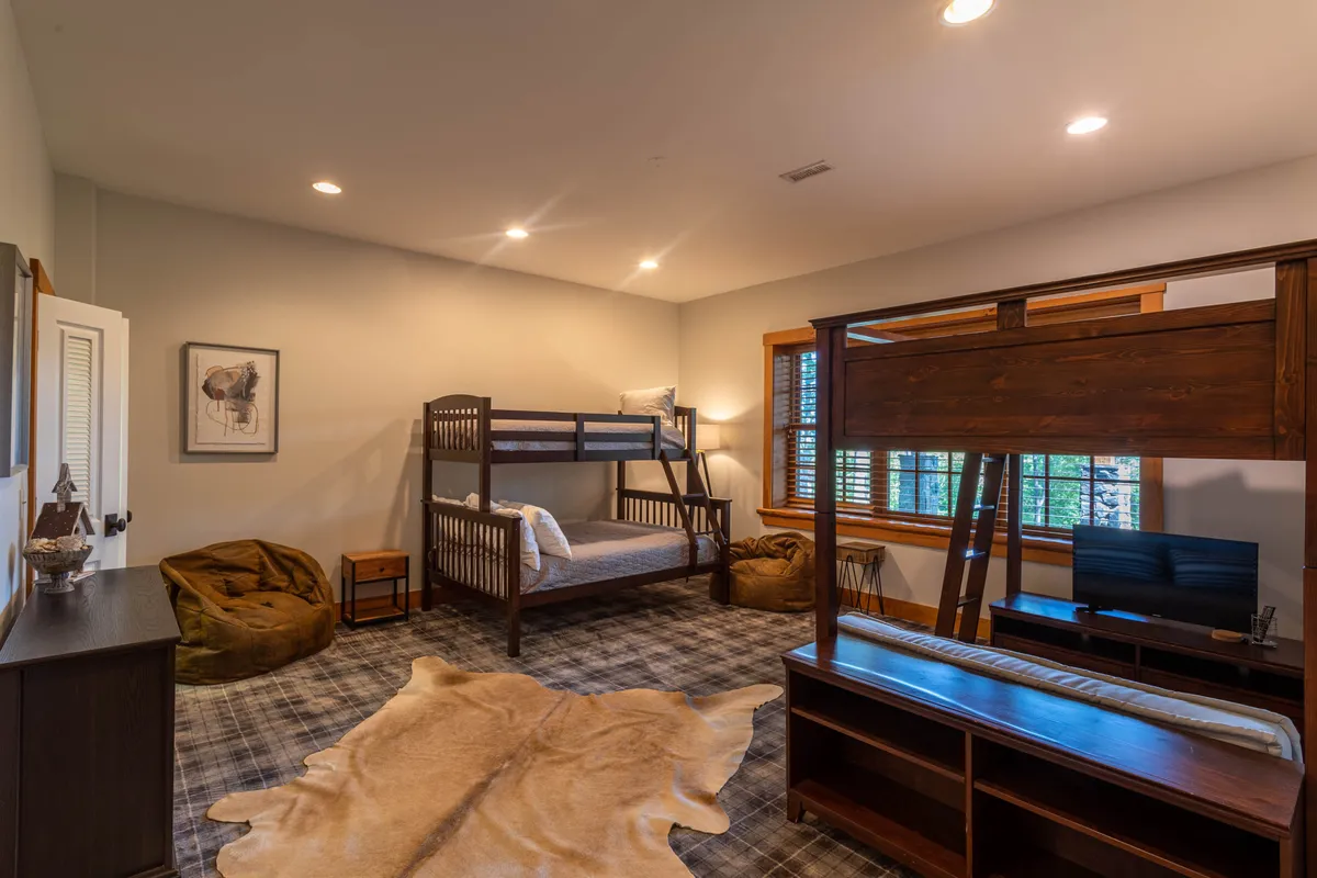 The image showcases a large, playful kids' bunk room with cozy bunk beds, colorful bean bag chairs, a TV, and cheerful artwork adorning the walls. The space is designed for both restful sleep and fun, perfect for children or sleepovers.