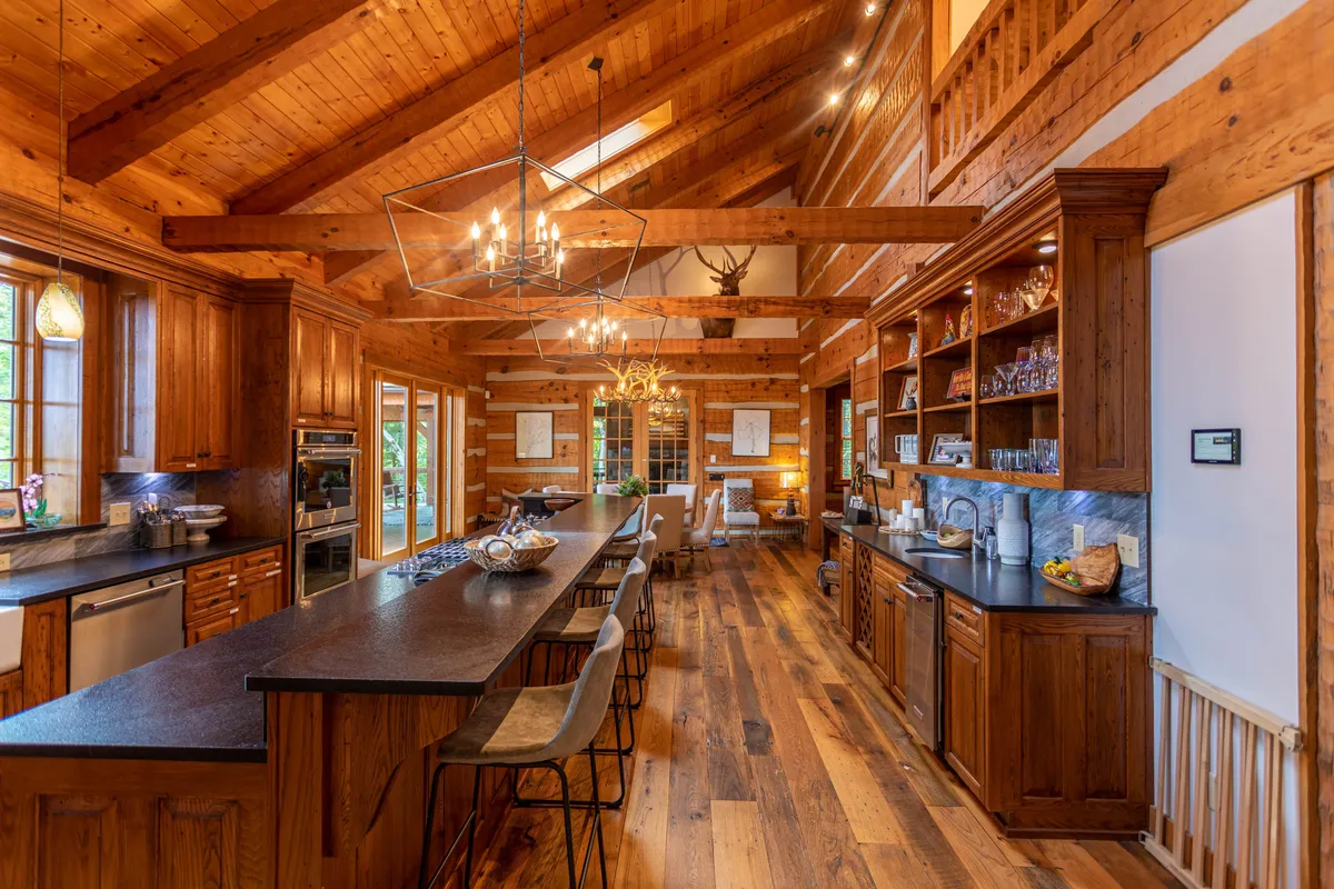A beautifully appointed kitchen with a generous island, wood cabinetry, a striking chandelier, and large windows framing lush outdoor views. The open layout is perfect for both cooking and gathering, with plenty of space for entertaining.