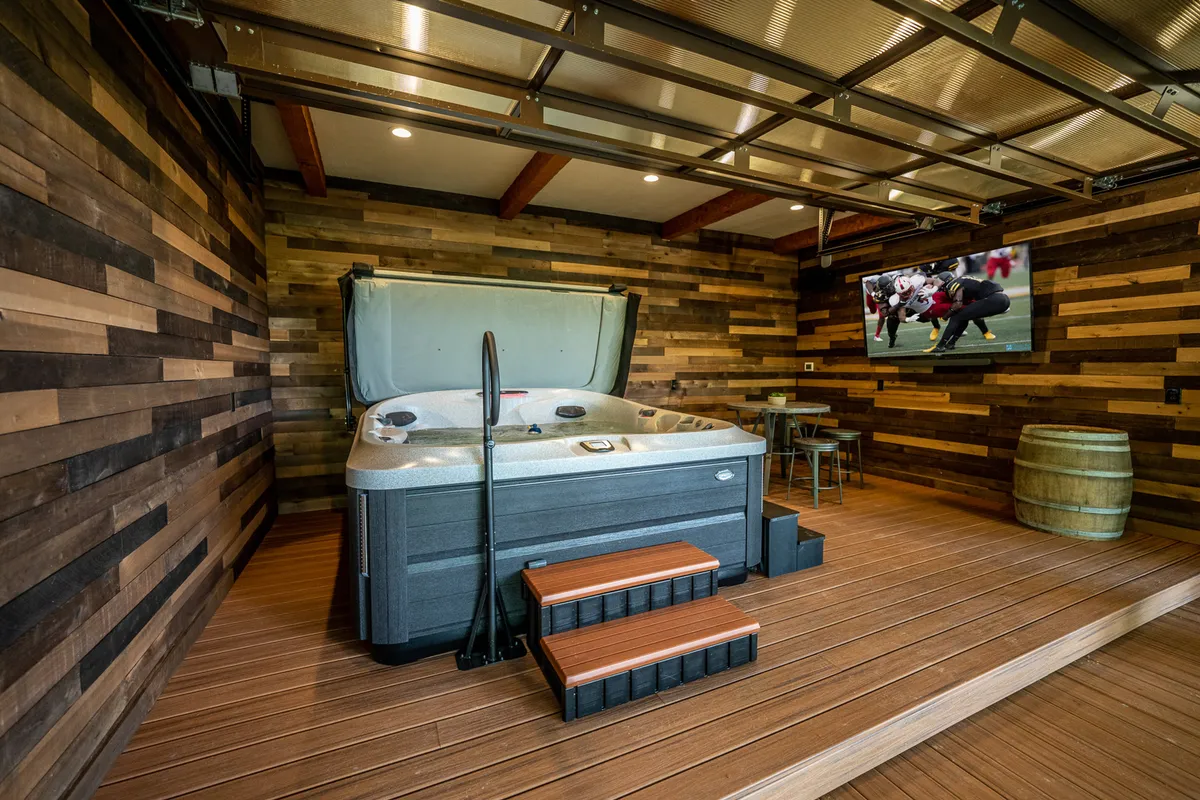 An inviting interior hot tub room with wood-paneled walls, a flat-screen TV, and a barrel table. The hot tub is the centerpiece, offering a cozy spot for relaxation after days spent exploring outside, and the space feels perfect for unwinding with family or friends.
