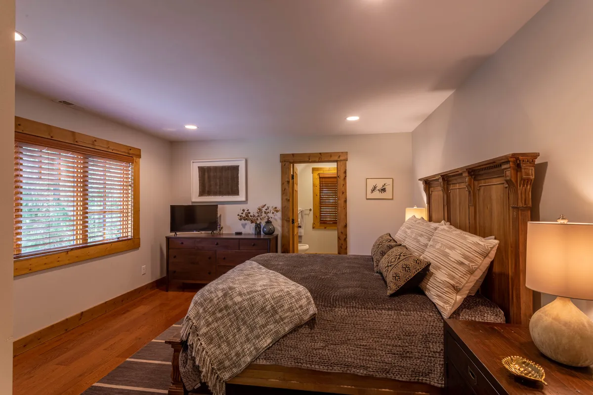 A cozy, inviting guest bedroom with a neatly made bed, nightstand, decorative lamp, and television. Warm tones and soft lighting create a welcoming ambiance ideal for privacy and comfort.