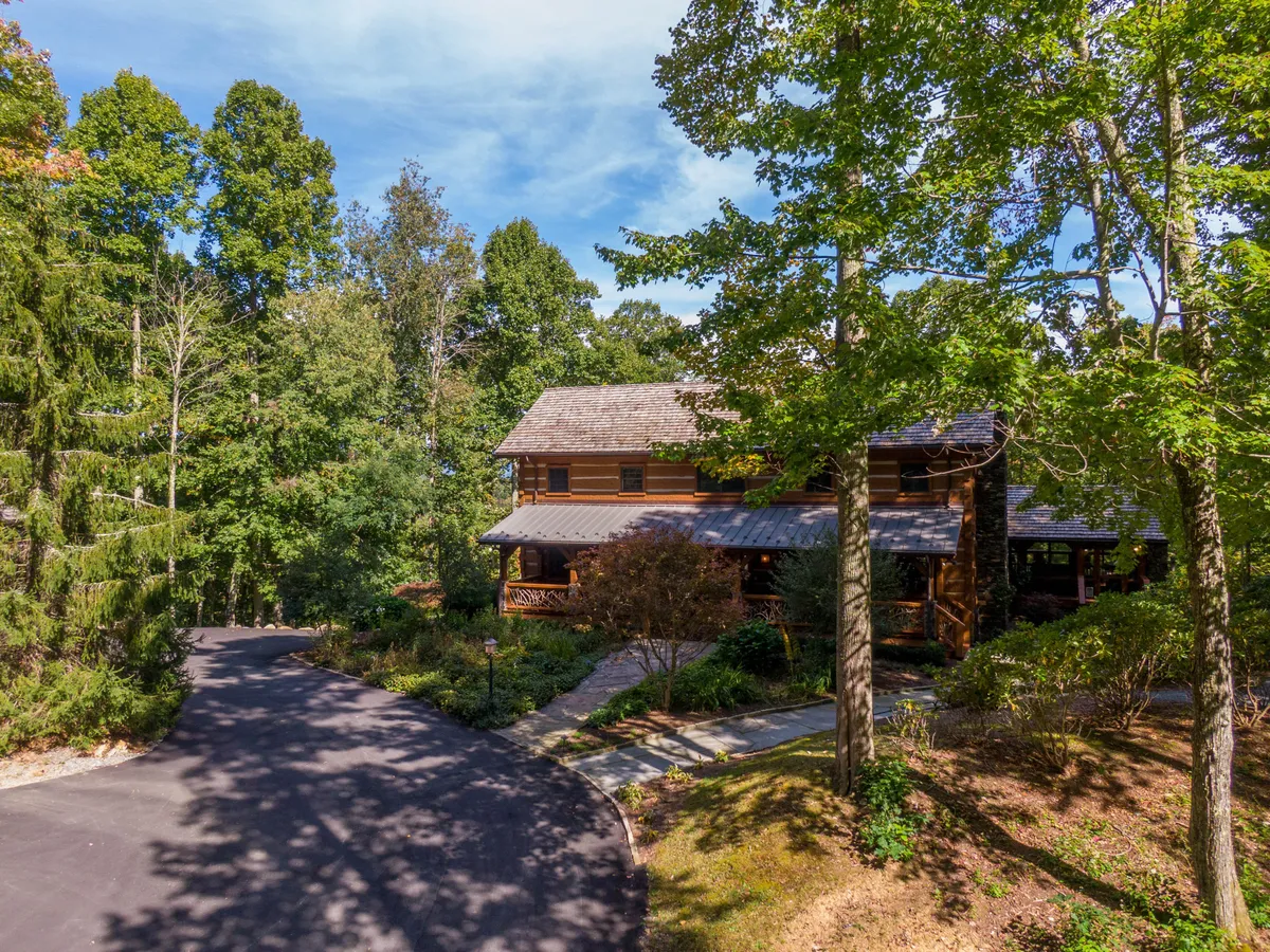 The hero image showcases a stunning wooden estate nestled amongst lush greenery, with a winding driveway leading up to the home. Expansive porches invite guests to relax and take in sweeping High Country views, while the secluded, tranquil setting hints at endless opportunities for outdoor adventure and serene gatherings.